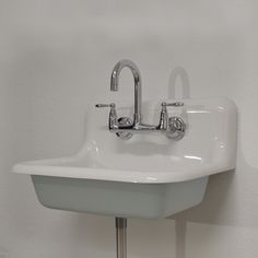 a white sink mounted to the side of a wall with two faucets on it