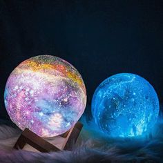 two colorful moon lamps sitting next to each other on a fur covered surface in front of a black background