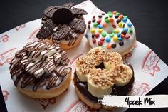 there are four donuts with different toppings on the paper wrapper and one has chocolate, sprinkles, and pretzels