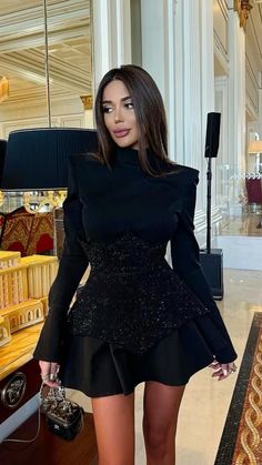 a woman standing in front of a mirror wearing a black dress and high heeled boots