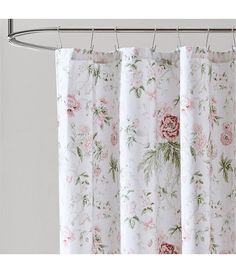 a white shower curtain with pink and green flowers on it, hanging from a metal rod