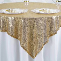 two white plates with gold sequins sit on top of a round table cloth