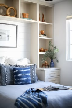 a bed with blue and white pillows on top of it next to a book shelf