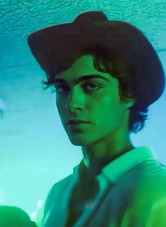 a young man wearing a black hat and green shirt is standing in front of a blue background