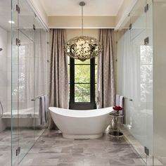 a bathroom with a tub, chandelier and glass walls