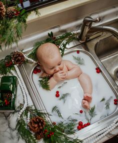 a baby is taking a bath in a sink with christmas greenery on the edge