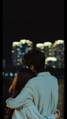 a man and woman embracing in front of a city skyline at night with lights reflecting off the water