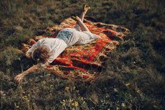 a woman laying on top of a rug in the middle of a grass covered field