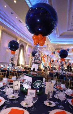 the table is set for an event with orange and blue balloons hanging from the ceiling