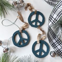 three wooden peace signs hanging from a christmas ornament on a white table with ornaments