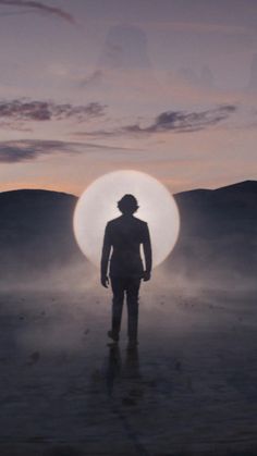 a man standing in the middle of a desert at night with a large round object behind him