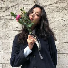 a woman is holding a rose in front of her face