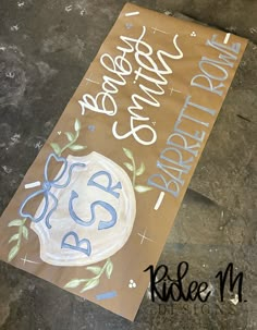 a brown paper bag with blue and white lettering on it sitting on the ground next to a sign