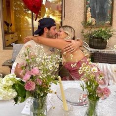 a man and woman embracing each other at a table with flowers in vases on it