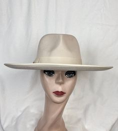 This beige felt flat brim 4-inch fedora with pinched fedora crown has a 1  1/2 inch grosgrain ribbon with a bow around the crown and an elastic tie in the crown which will fit up to 22 7/8 inch head size. The inside band has a sizing cord to adjust to your head size. The brim has a ribbon edging. NOTE: Please check the head size before purchase, I am happy to answer any questions you may have. There will be a 20% restocking fee for all returned hats. Cream Fedora Panama Hat For Kentucky Derby, Classic Beige Fedora With Flat Brim, Classic Beige Flat Brim Fedora, Elegant Beige Fedora With Flat Crown, Formal Beige Fedora With Short Brim, Classic Beige Fedora Felt Hat, Cream Fedora Hat For Formal Occasions, Fitted Cream Panama Hat Fedora, Fitted Beige Fedora With Flat Brim