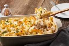 a casserole dish filled with chicken and pasta being held by a wooden spoon