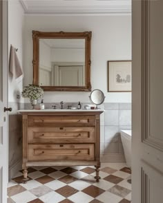 a bathroom with a checkered floor and white walls, an old fashioned wooden vanity has a large mirror above it