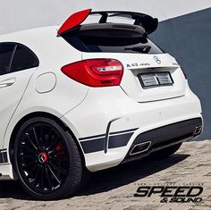 the rear end of a white car parked in front of a gray and black wall