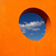 an orange wall with a round hole in the middle and a blue sky behind it