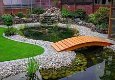 a wooden bridge over a small pond in a garden with rocks and grass around it