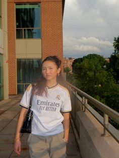 a young woman walking down a sidewalk next to a tall brick building with trees in the background