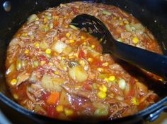 a pot full of food with a spoon in it and some corn on the side