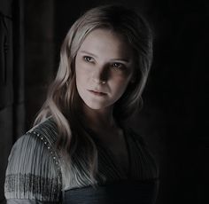 a woman with long blonde hair and blue eyes is looking at the camera in a dark room