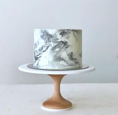 a marbled cake on a wooden stand with white and black icing, sitting on a table