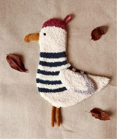 a knitted bird laying on top of a bed next to leaves and acorns