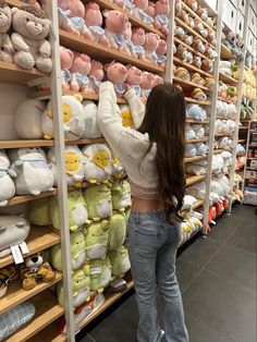 a woman is looking at stuffed animals on display in a store with shelves full of stuffed animals