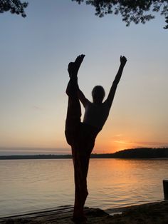 a woman doing yoga on the beach at sunset with her hands up in the air