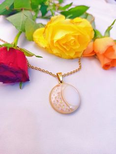 a necklace with a crescent moon and stars on it next to some yellow rose buds