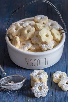 a white bowl filled with cookies and powdered sugar on top of a blue table