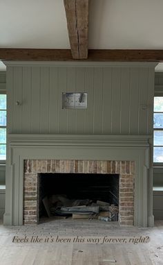 an empty room with a brick fireplace and wood beams on the ceiling is painted green