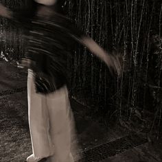 black and white photograph of a woman holding an umbrella in front of a bamboo fence