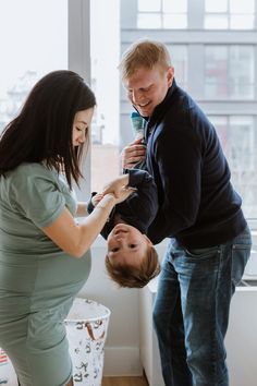 a man and woman standing next to each other in front of a window with a baby on his belly