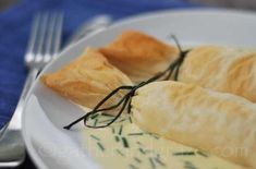 two croissants on a white plate with cream sauce and green sprigs