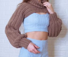 a woman in a blue top is wearing a brown knitted sweater and has her hands on her hips