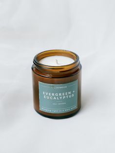 a candle that is sitting on a white surface with the words evergreen eucalyptus plus in front of it