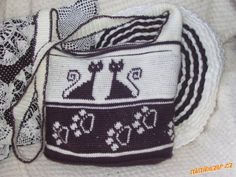 a white and black handbag sitting on top of a bed next to a lace doily