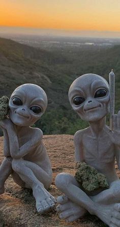 two alien figurines sitting on top of a hill with a knife in their hands