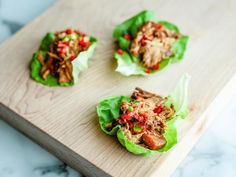 three lettuce wraps filled with meat and vegetables on a cutting board next to a knife