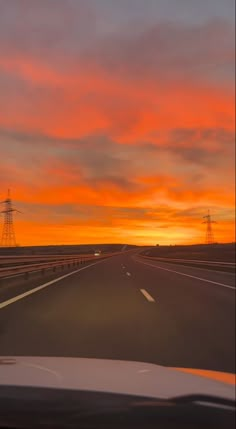 the sun is setting on an empty highway with power lines in the distance and orange clouds