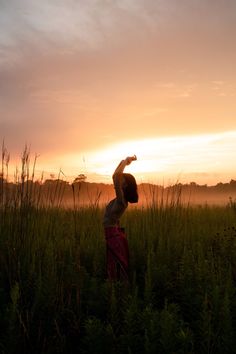 a woman standing in the middle of a field with her arms up to the sky