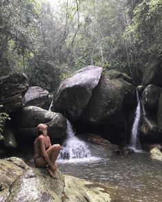 a woman sitting on top of a rock next to a waterfall