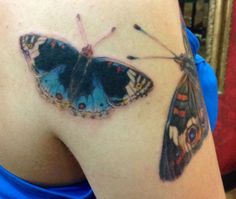 a butterfly tattoo on the back of a woman's left shoulder, with blue and black wings