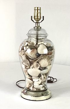 a glass vase filled with sea shells on top of a white table next to a lamp