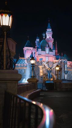 the disneyland castle is lit up at night with its lights on and some buildings in the background