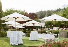 tables and chairs with umbrellas set up for an outdoor wedding reception in the garden