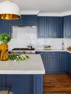 a kitchen with blue cabinets and marble counter tops, gold pendant light over the stove